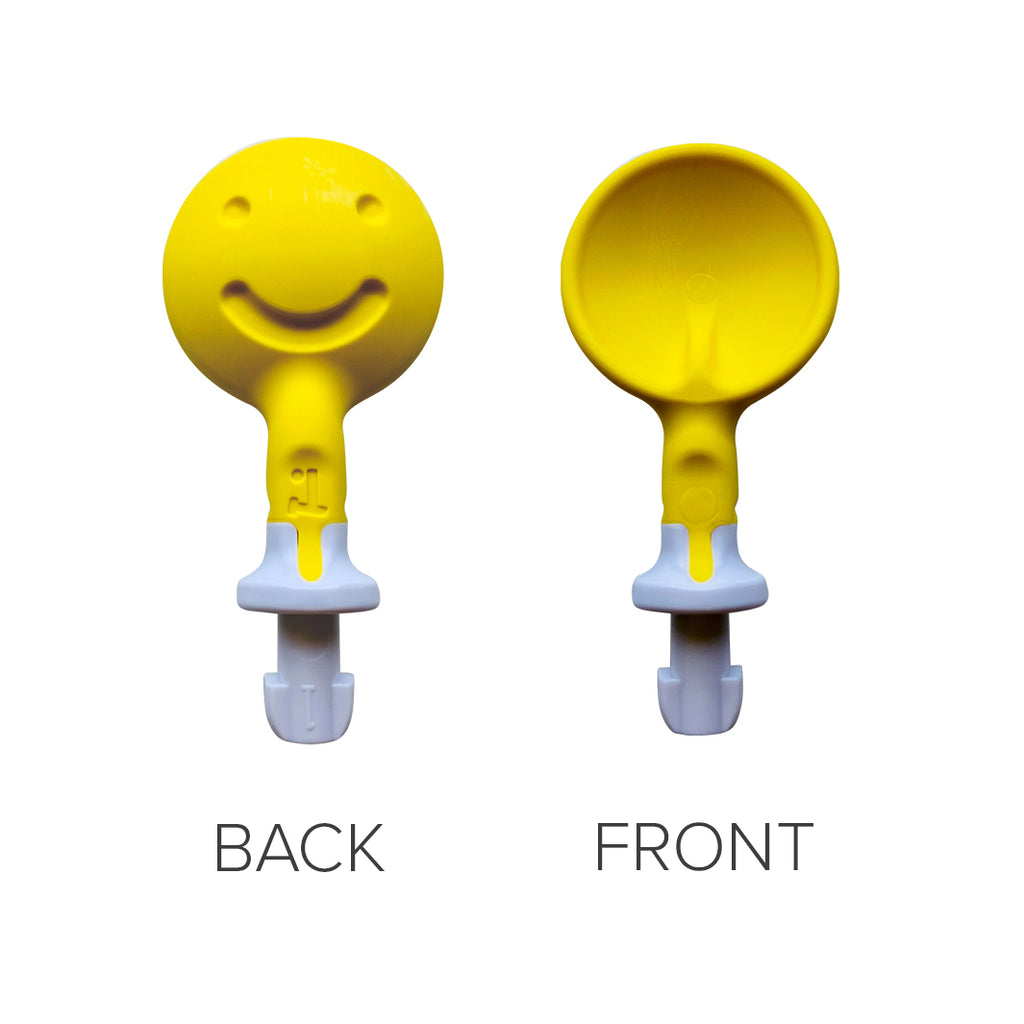 Front and back views of a yellow TalkTools Sensi Smiley Tip with a round smiley face and a spoon-shaped side.