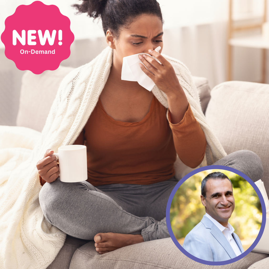 A woman sitting on a couch, wrapped in a blanket, holding a mug and tissue, with a man’s photo in the corner.