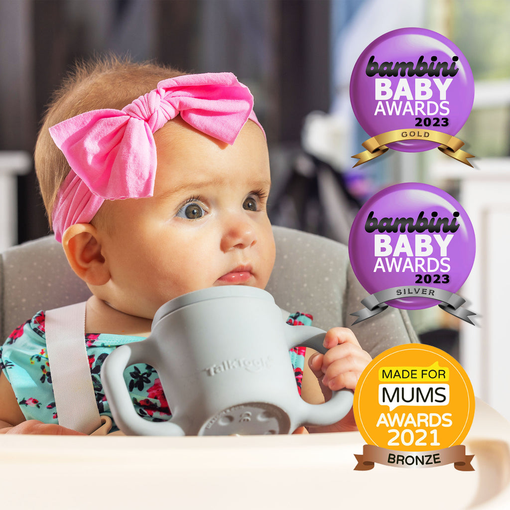 TalkTools Itsy Cup in gray held by a baby wearing a pink bow headband, with award badges in the background.