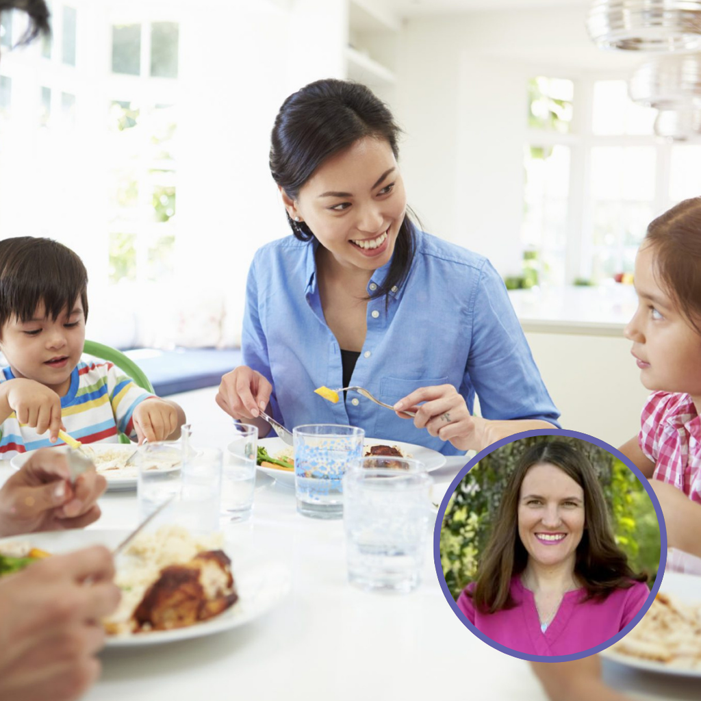 A woman in a blue shirt engages with children at a dining table, sharing a meal with plates and glasses visible.